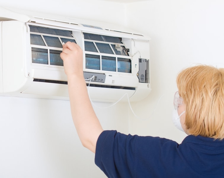 Woman checking unit to help maintain her ductless heating & cooling system