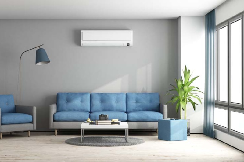 Ductless Mini Splits for Comfortable and Healthy Living. Image shows a blue and gray modern living room with sofa and air conditioning ductless unit on wall.