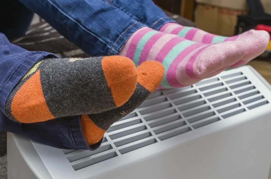 homeowners with their feet over the furnace trying to stay warm after following the furnace maintenance tips